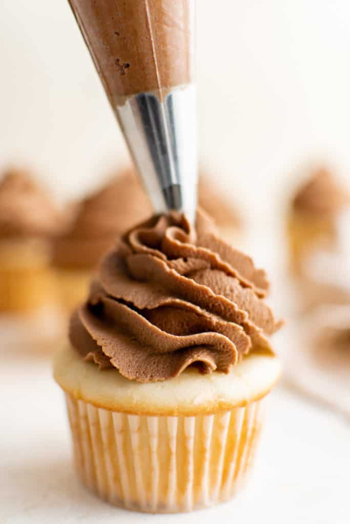 Piping bag adding chocolate hazelnut frosting to a cupcake.