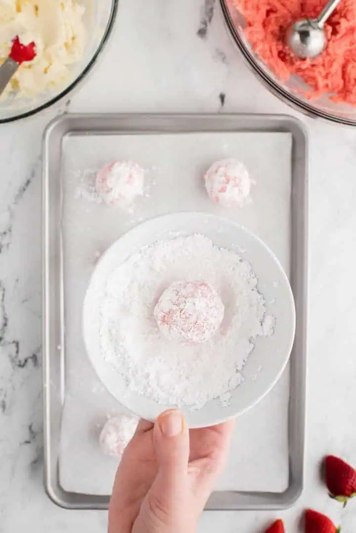 Cookie dough ball in a bowl of powdered sugar.