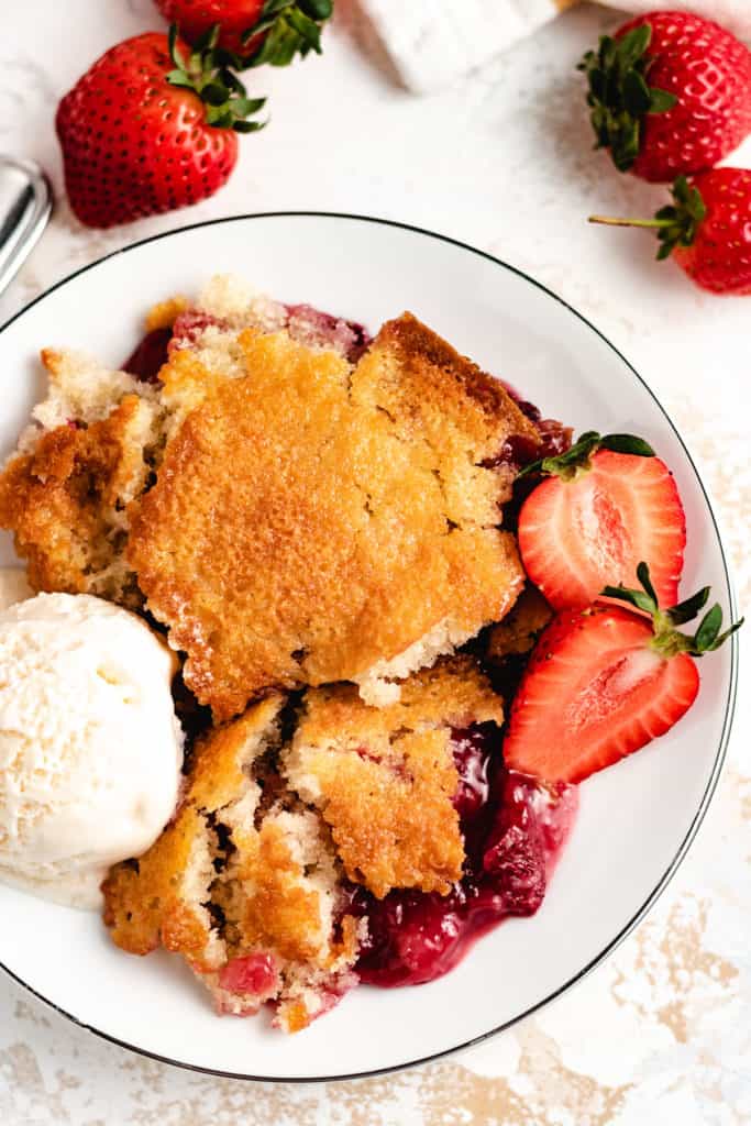 Top down view of scoops of strawberry cobbler on a white dish.