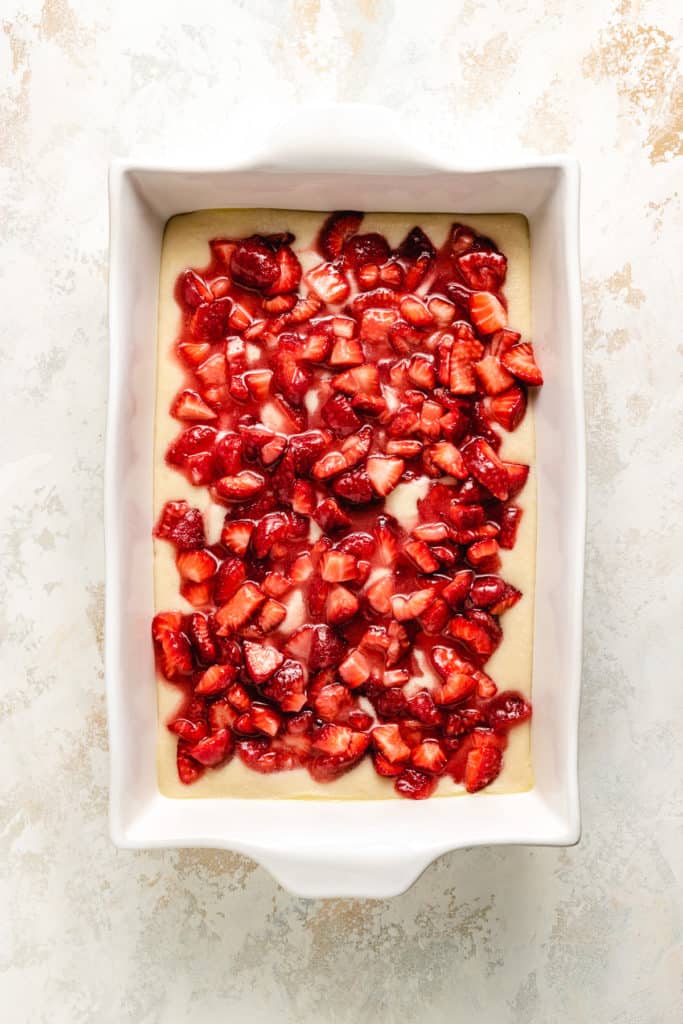Strawberries layered over cobbler batter in a dish.