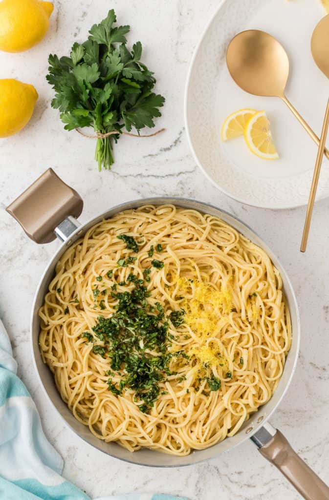 Fresh basil and lemon zest added to pasta in a pan.