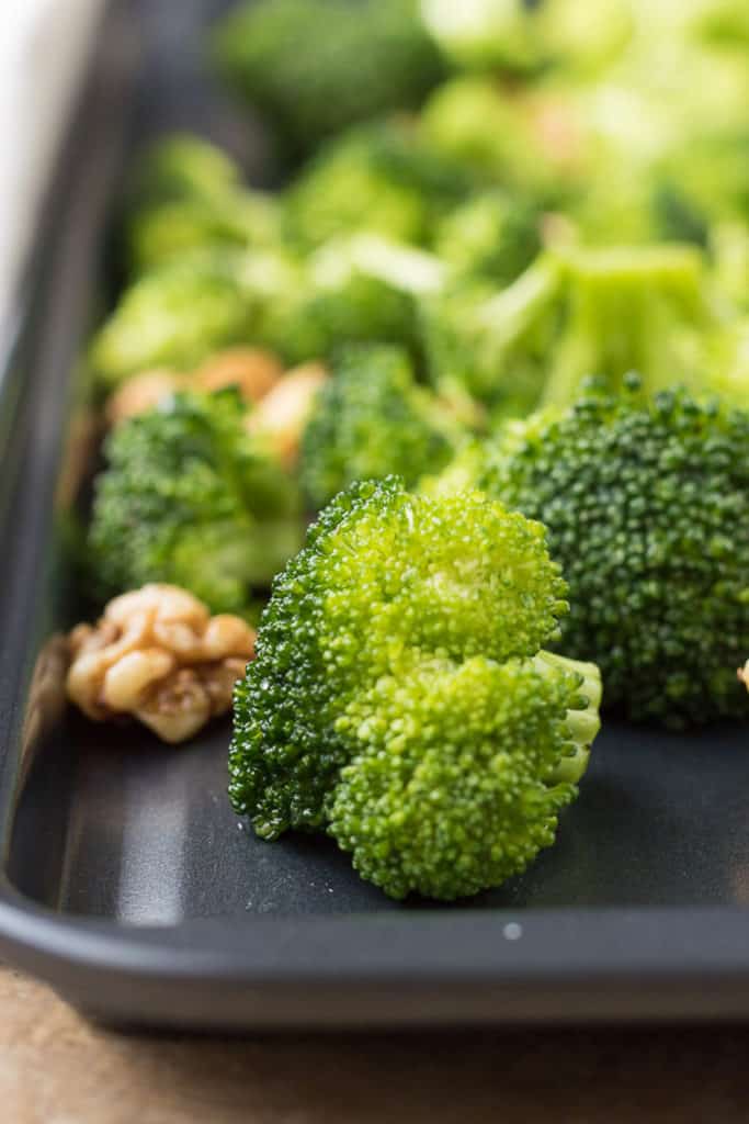 Broccoli florets and walnuts on a sheet pan.