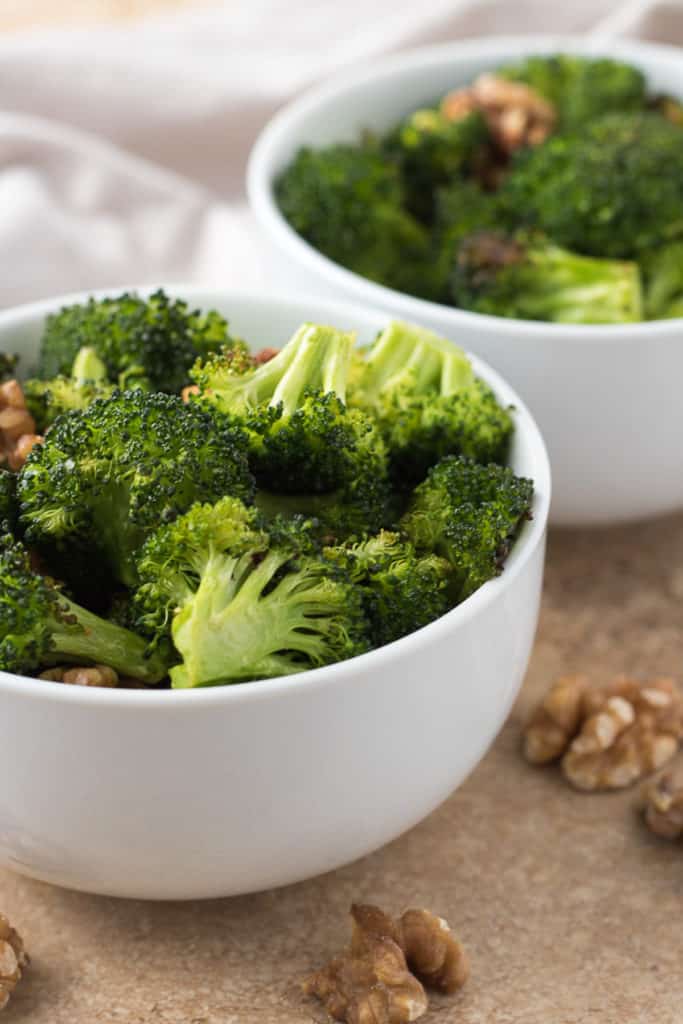 Two white bowls filled with roasted broccoli.