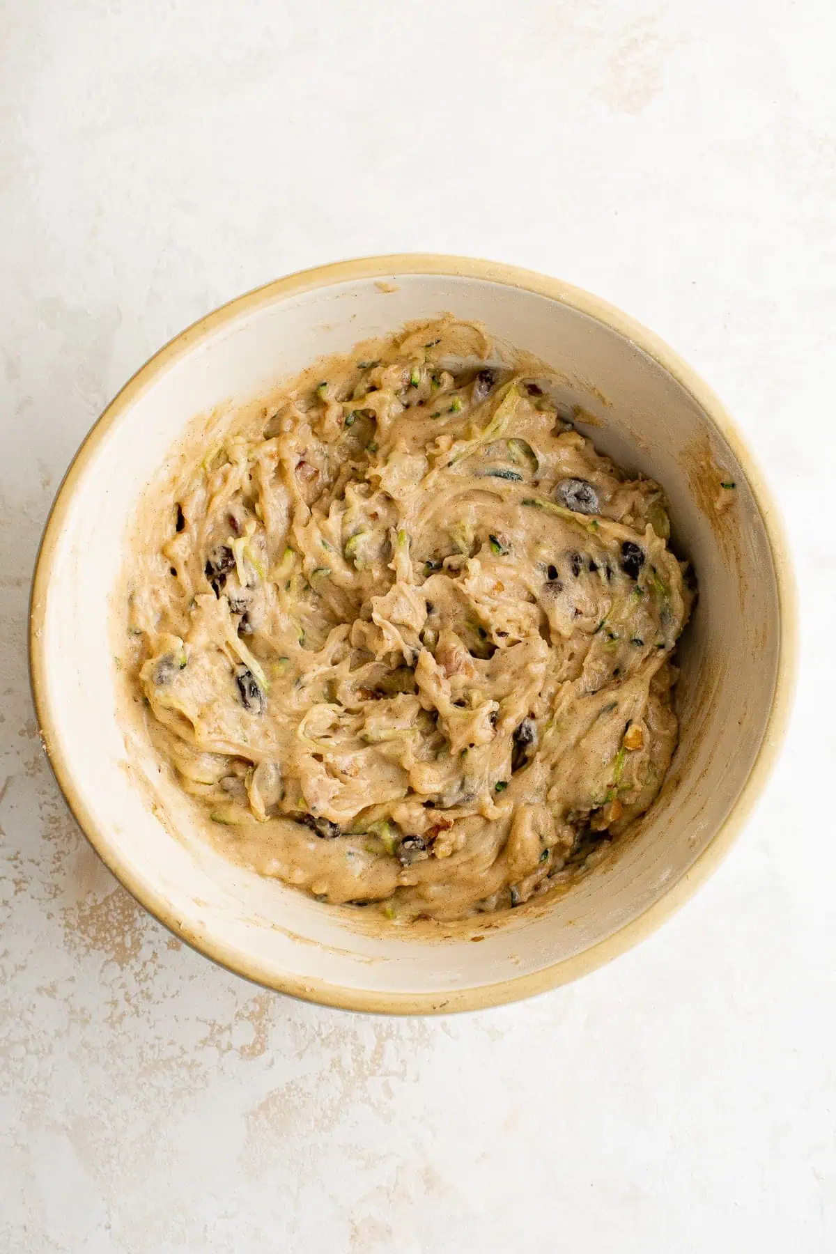 Zucchini bread batter, raisins and nuts stirred in a bowl.