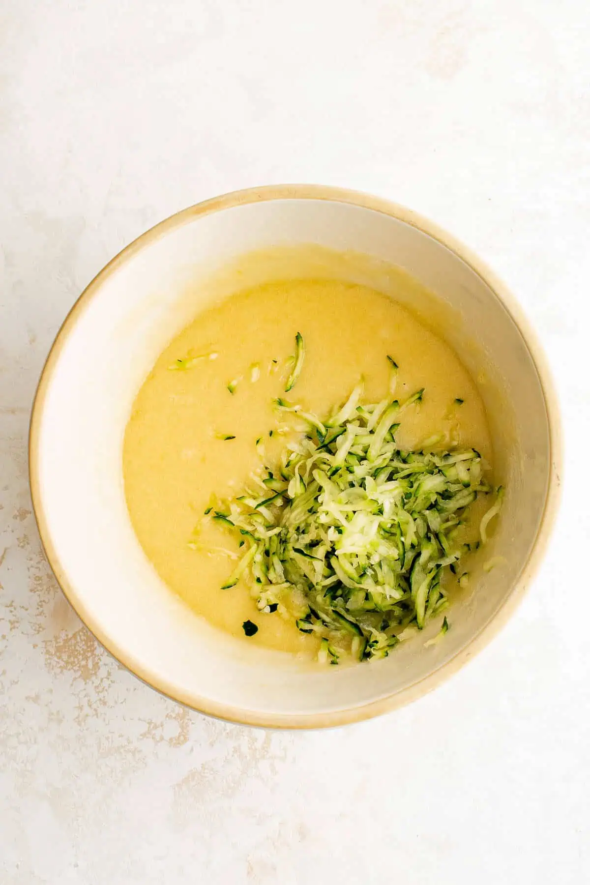 Eggs, sugar, butter and vanilla in a bowl with zucchini.