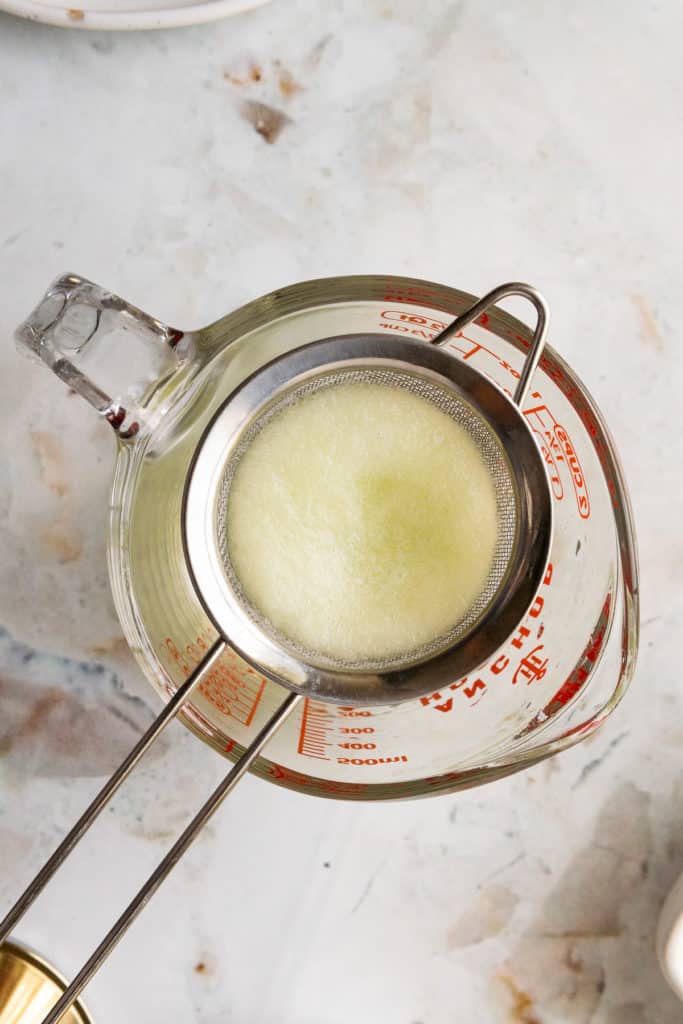 Cucumber juice being poured through a strainer.