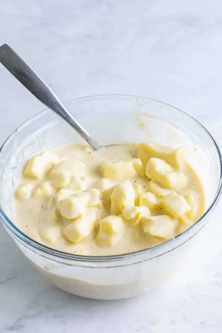 Cheese curds soaking in a bowl of batter.