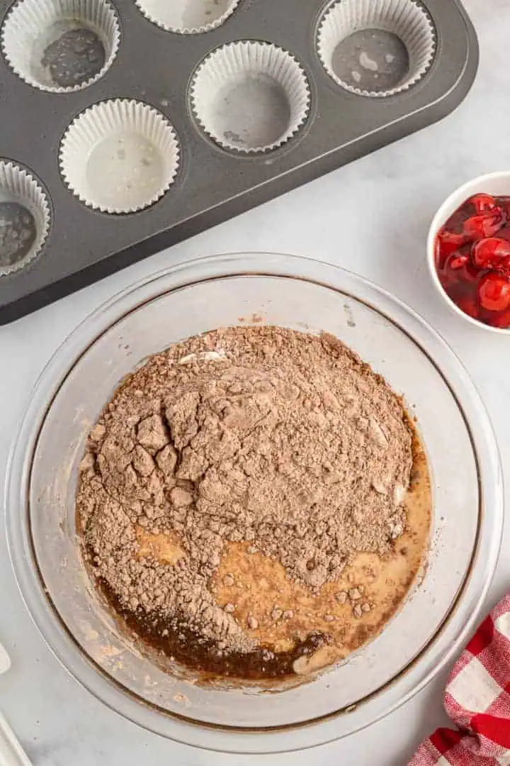 Cocoa powder and flour mixture added to a bowl of eggs and oil.