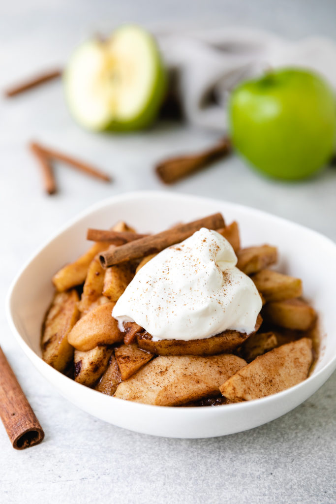 White dish filled with crock pot cinnamon apples and whipped cream.