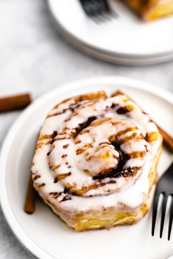 Angled view of a cinnamon roll with heavy cream on a plate.