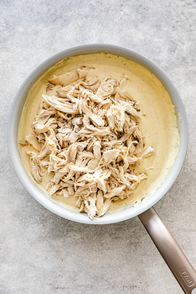 Shredded chicken in a pan with creamy sauce.