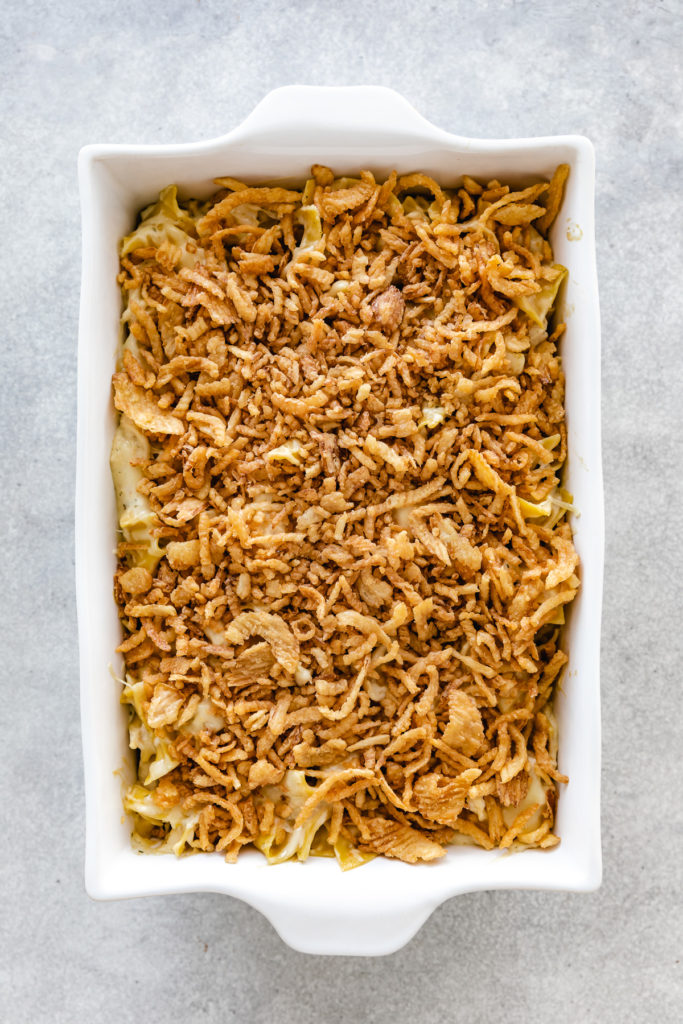 Top down view of crispy french fried onions being added to a casserole.