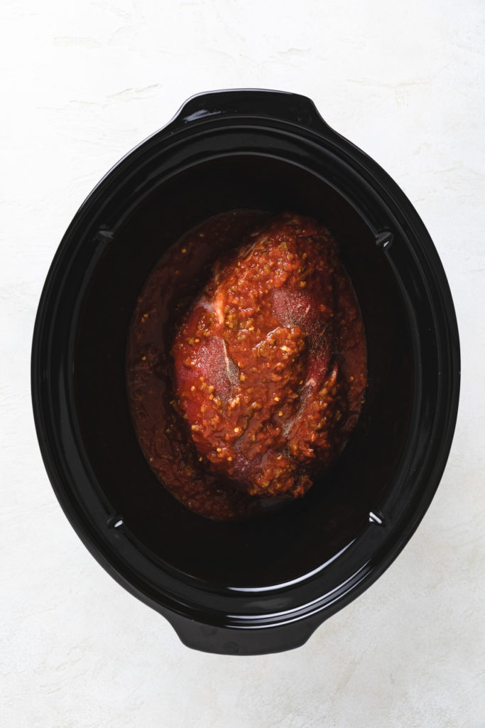 Salsa poured over a beef roast in a slow cooker.