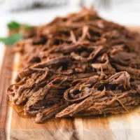 Slow cooker shredded beef on a cutting board.