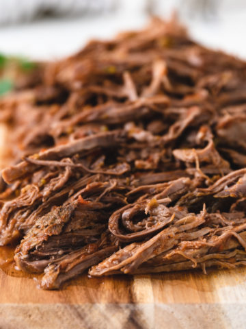 Slow cooker shredded beef on a cutting board.