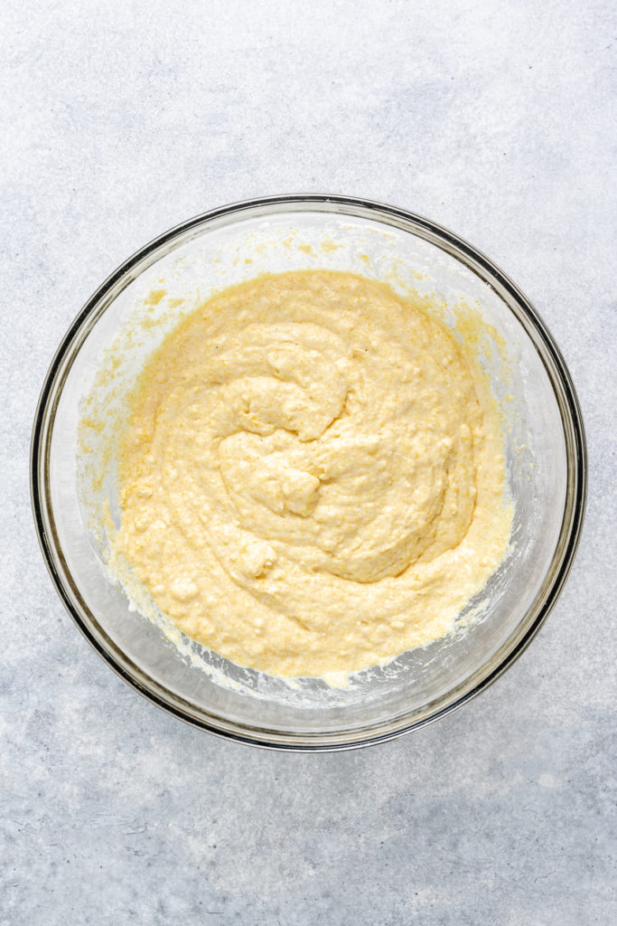 Unbaked cornmeal, milk, flour, eggs, and butter mixed in a bowl.
