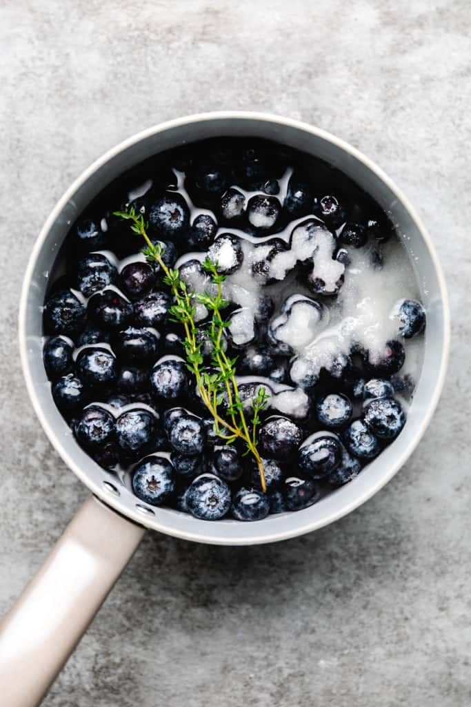 Blueberries, water, sugar, and thyme in a pan.