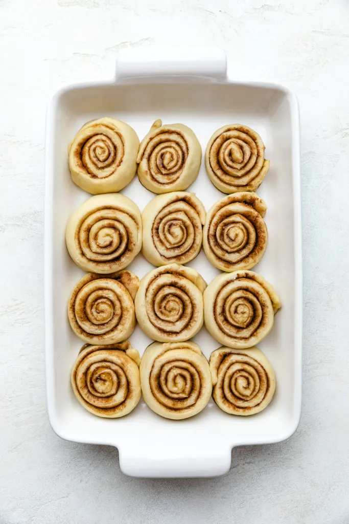Puffy cinnamon buns in a baking pan.