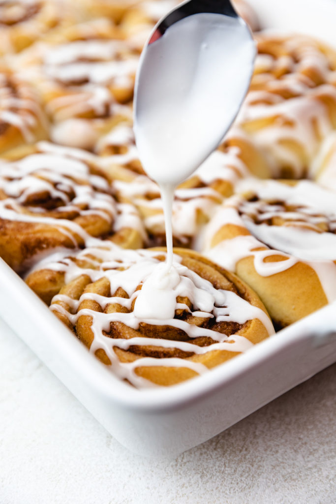 Sweet glaze being drizzled over cinnamon rolls.
