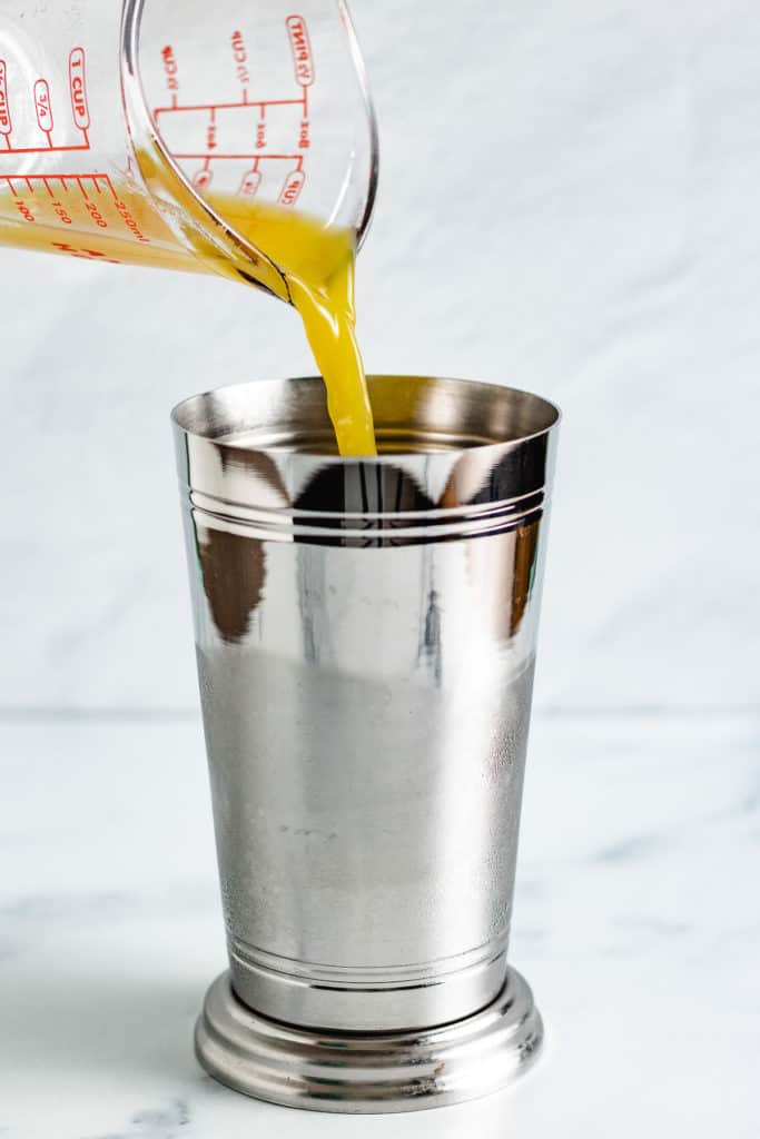 Orange juice being added to a metal drink shaker.