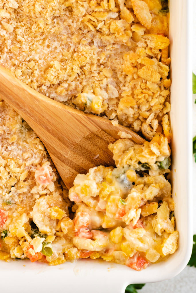 Wooden spoon scooping mixed vegetable casserole out of a dish.