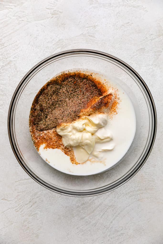 Spices poured into a bowl of milk, buttermilk, and mayo.