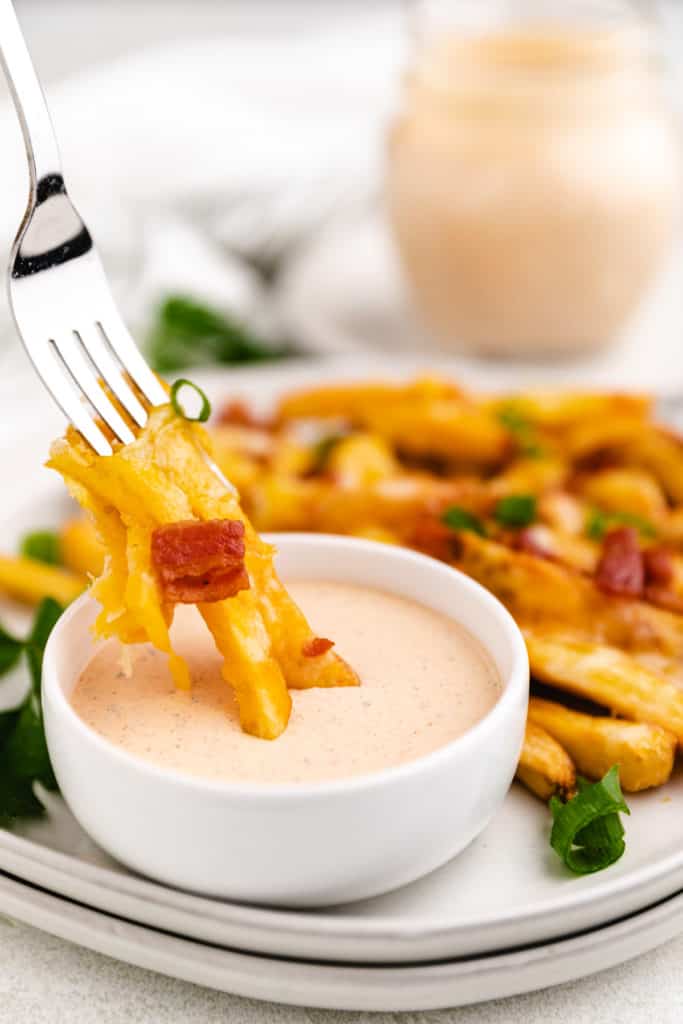Cheese fries being dipped into spicy ranch dressing.