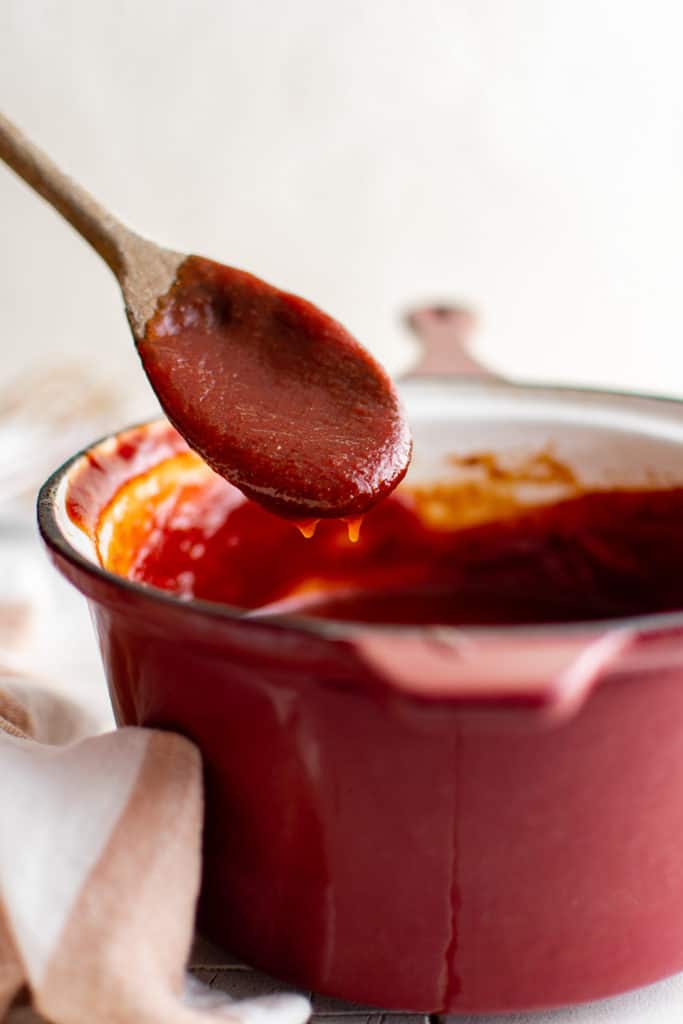 Wooden spoon stirring a pan of barbecue sauce.