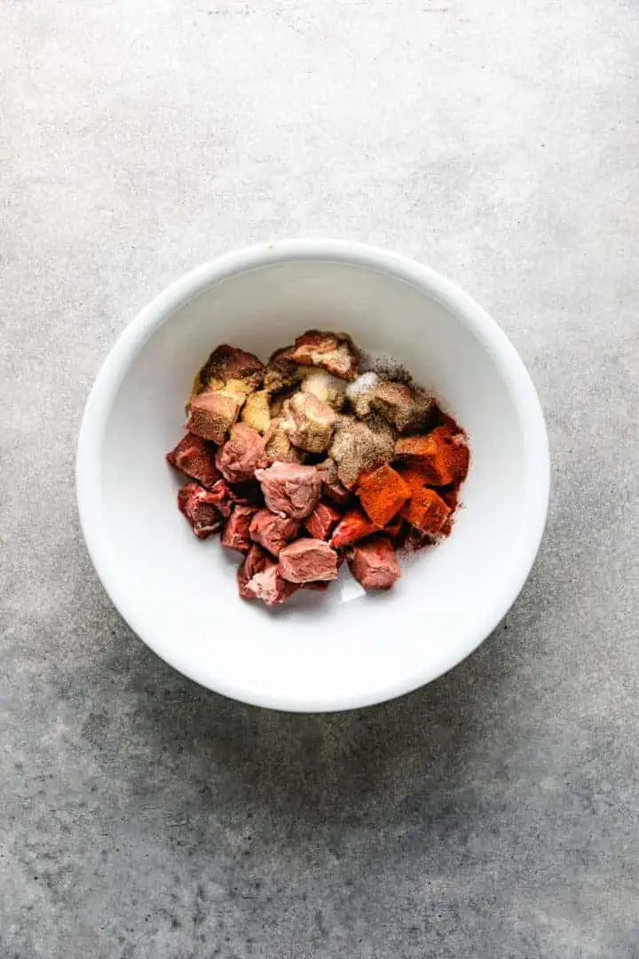 Cubed beef with savory seasonings in a white bowl.