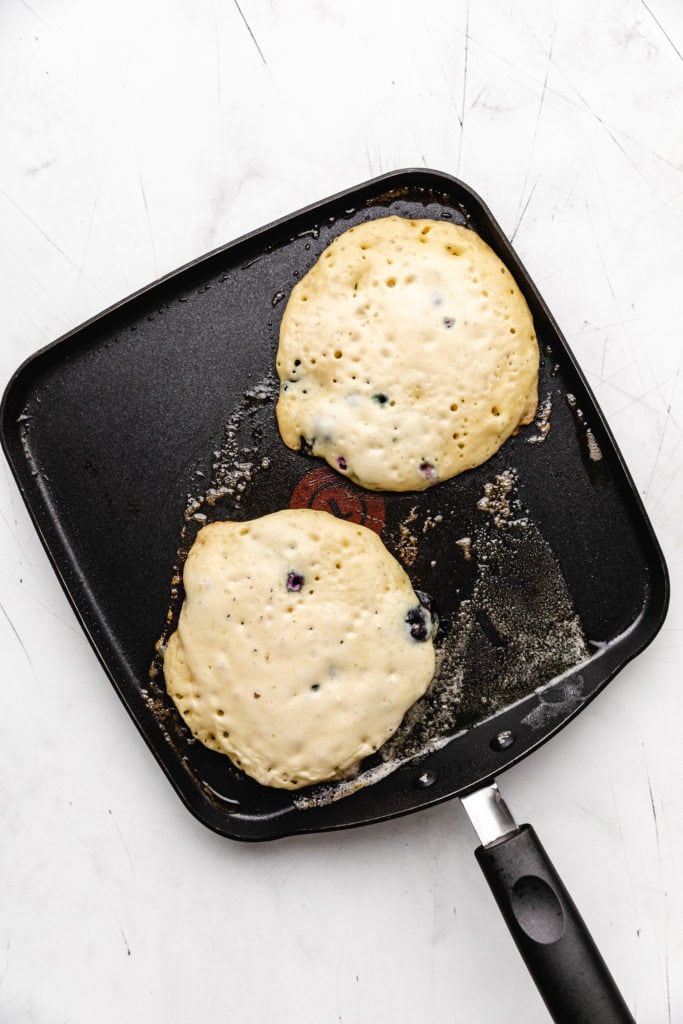 Blueberry pancakes cooking on a pan.