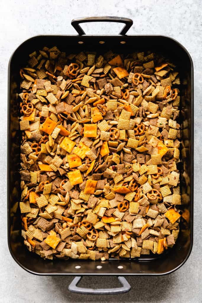 Seasoned cereal, peanuts, crackers, and pretzels in a roasting pan.