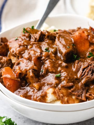 Side view of white bowls filled with mashed potatoes and Irish beef stew.