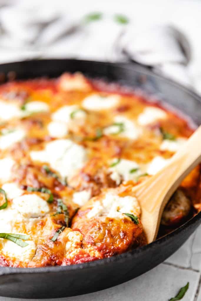Wooden spoon dipped into a casserole with meatballs.
