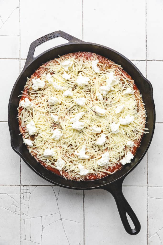 Ricotta and mozzarella sprinkled over a pan of meatballs and marinara.