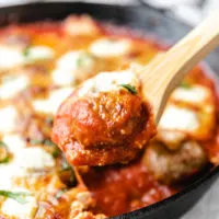 Wooden spoon holding a cheesy baked meatball.