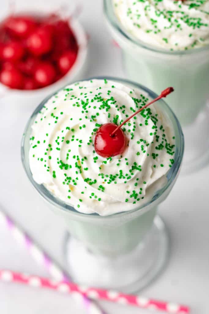 Top down view of a cherry and sprinkles on a green milkshake.