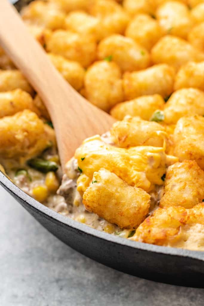 Wooden spoon scooping cheesy potato puff casserole.