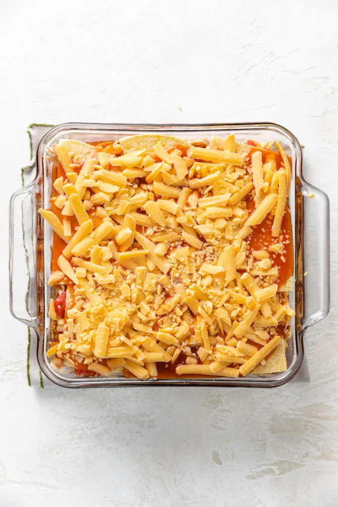 Shredded cheese added to an enchilada casserole.