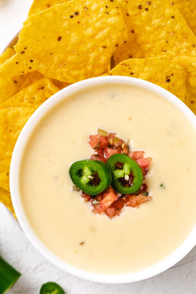 Top down view of diced tomatoes and jalapenos on a bowl of cheese dip.