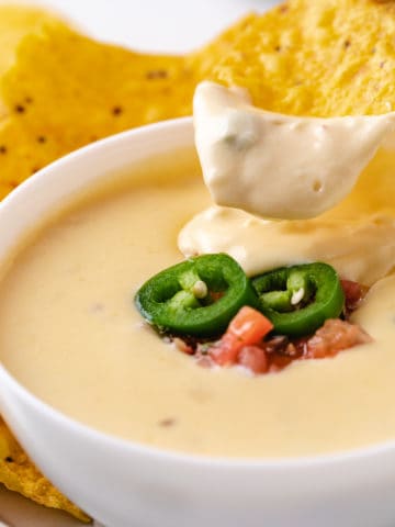 Close up view of a chip dipping into a bowl of cheese dip.