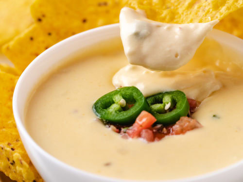 Close up view of a chip dipping into a bowl of cheese dip.