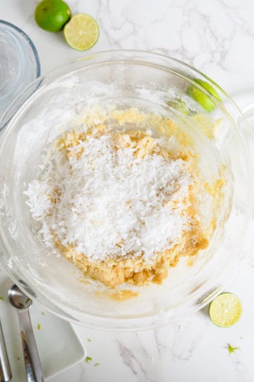 Shredded coconut added to a bowl of cookie dough.