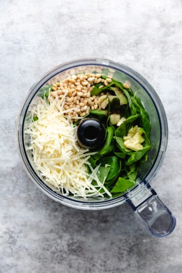 Top down view of ingredients for pesto sauce in a food processor.