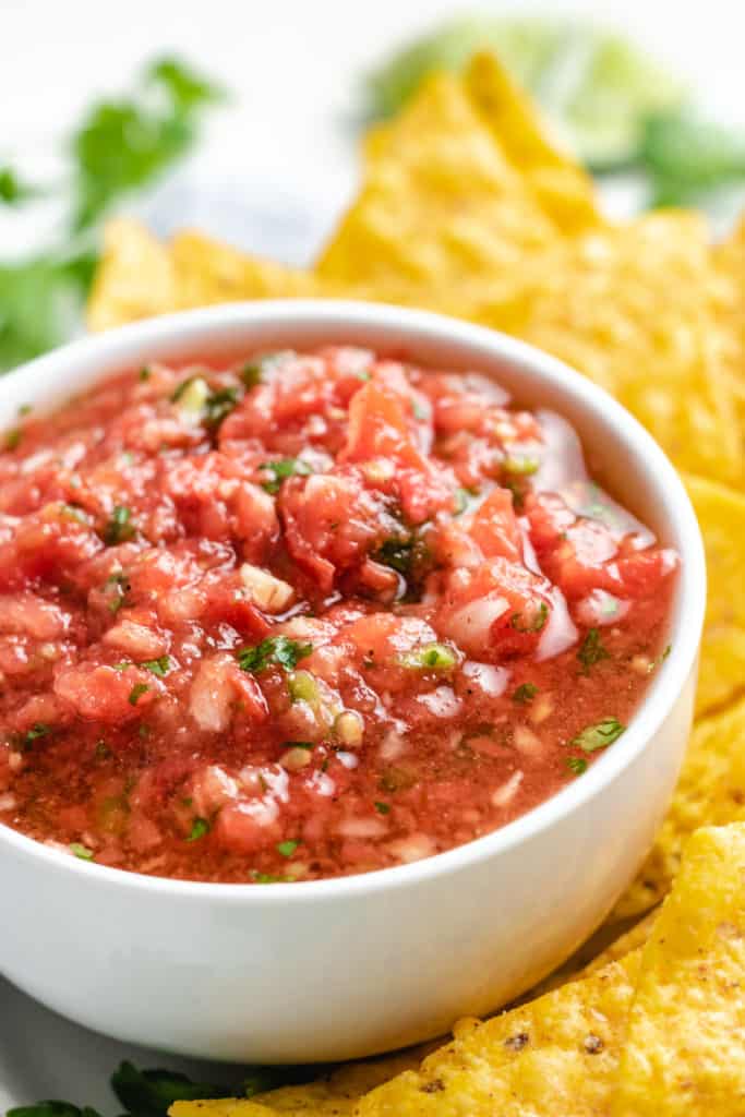 Salsa with fresh tomatoes next to tortilla chips.