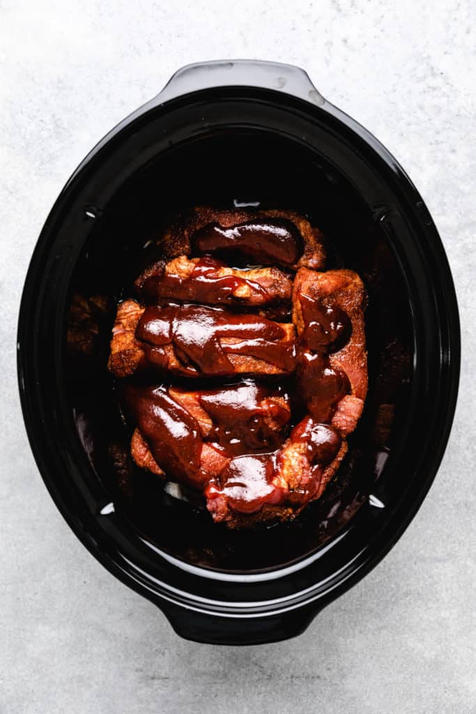 Bbq sauce on top of country style ribs in a slow cooker.