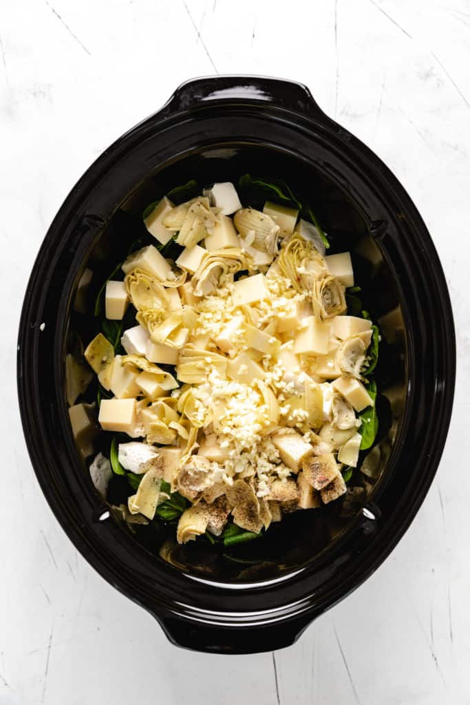 Top down view of spinach, cheese, sour cream, and cream cheese in a crockpot.