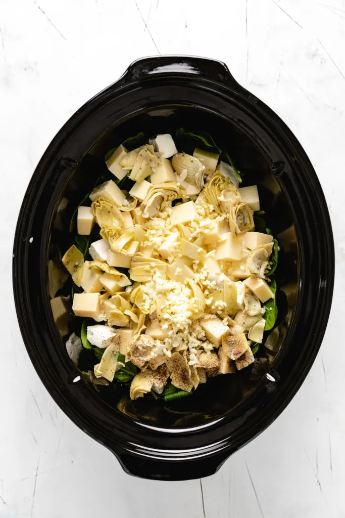 Top down view of spinach, cheese, sour cream, and cream cheese in a crockpot.