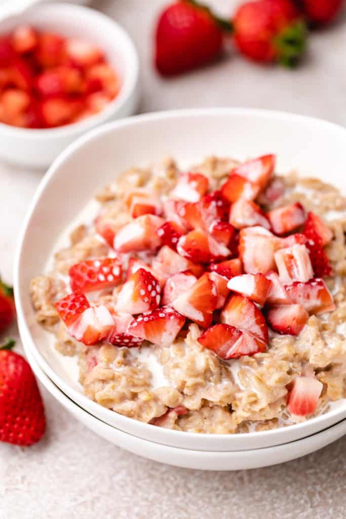 Two white bowls filled with oatmeal and strawberries.