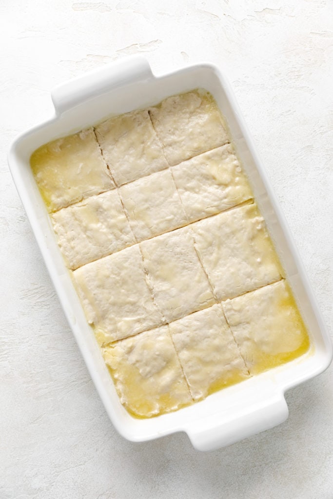 Unbaked biscuit dough in a pan of melted butter.