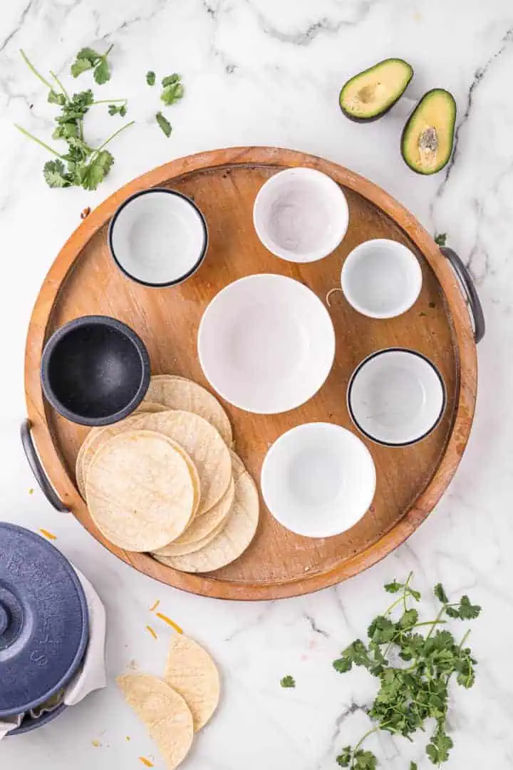 Tortillas and bowls on a wooden board.